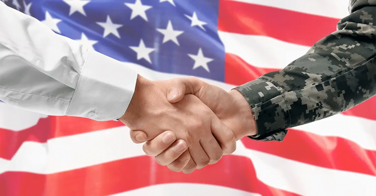 A soldier and civilian shaking hands with the USA flag in the background